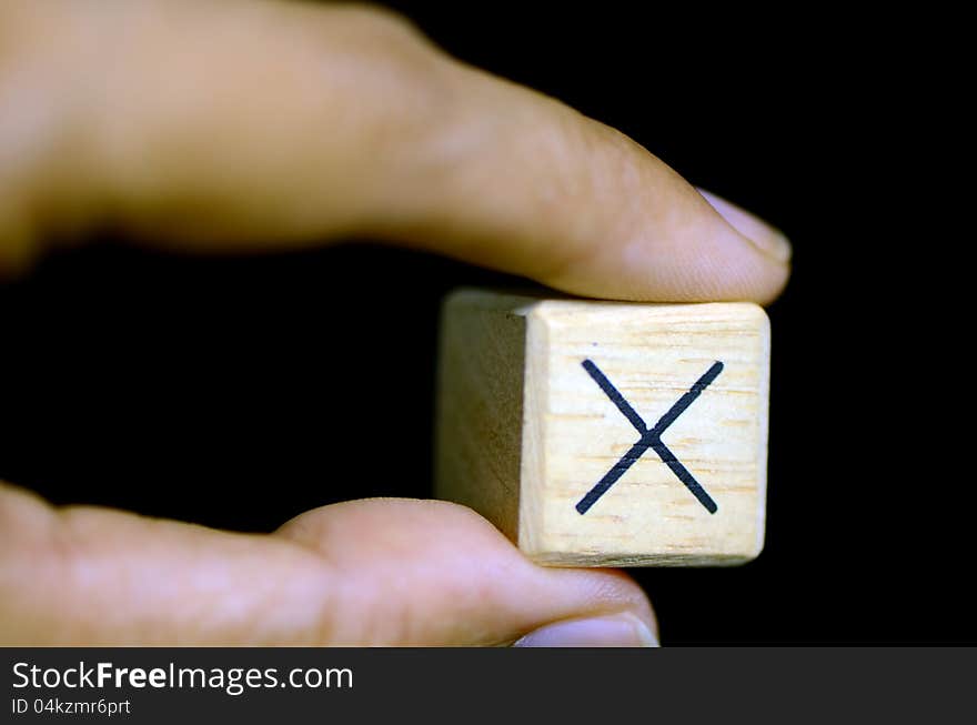 Left hand picking-up a wooden boxes with sign x on black background. Left hand picking-up a wooden boxes with sign x on black background.