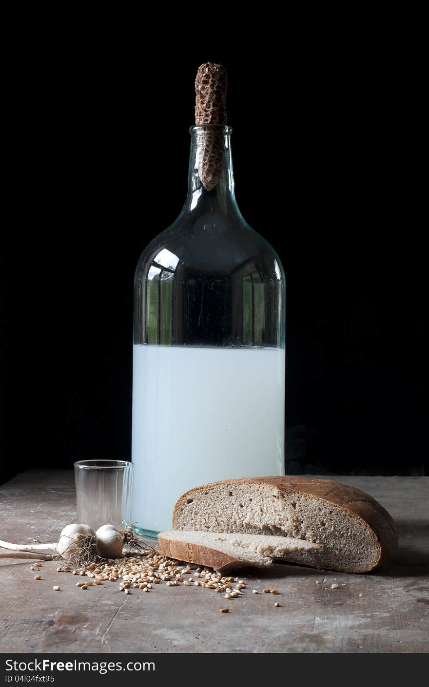 Old bottle with alcohol, wheat, corn, glass and garlic in a rustic cellar