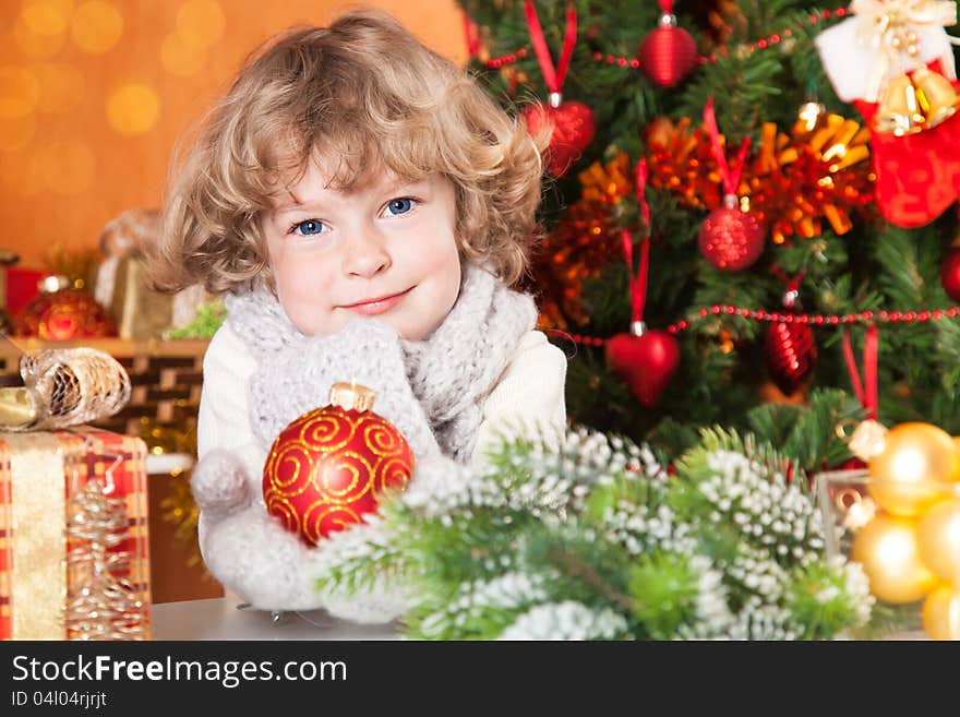 Happy child holding red ball against Christmas tree with decorations. Happy child holding red ball against Christmas tree with decorations