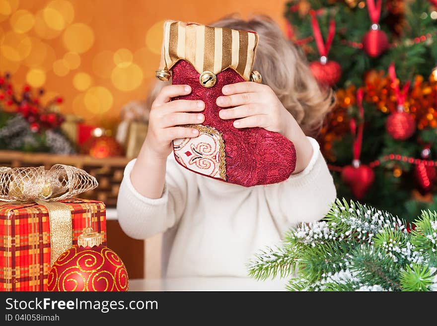 Funny child holding red sock against Christmas decorations background. Funny child holding red sock against Christmas decorations background