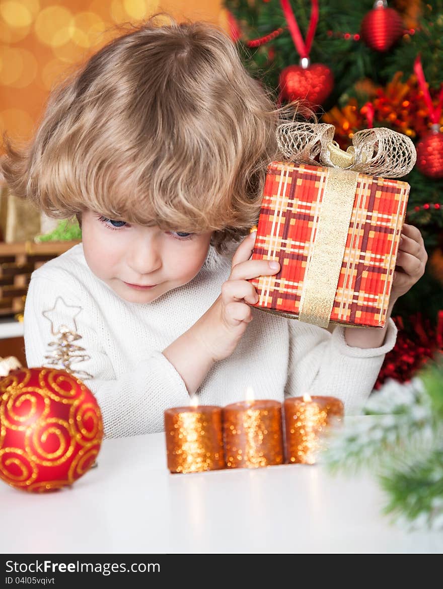 Funny child holding gift against Christmas tree with decorations