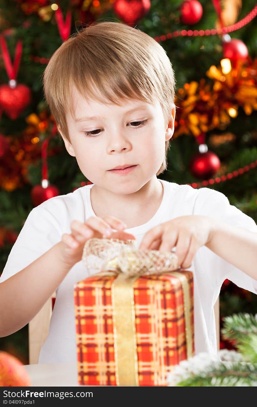 Surprised boy opening present against Christmas tree with decorations. Surprised boy opening present against Christmas tree with decorations