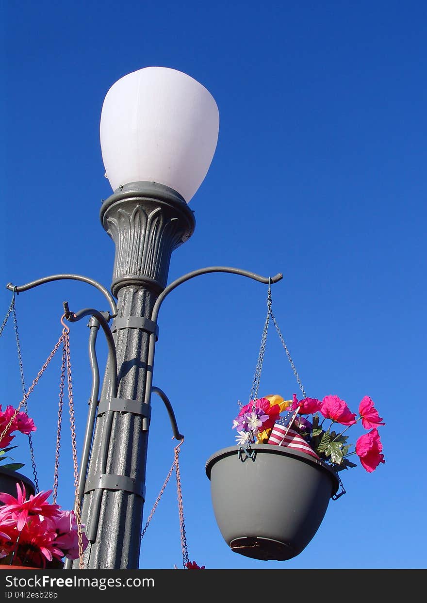 Abstract Concrete Retro Lamp Post against clear blue sky background with flower pots and flowers hanging