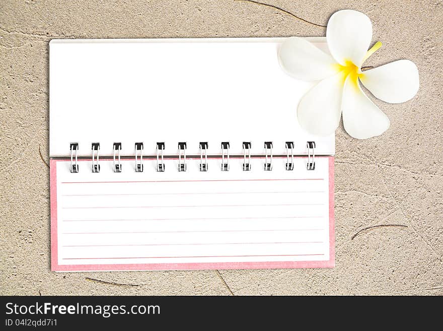White notebook with white Frangipani flower on the sand