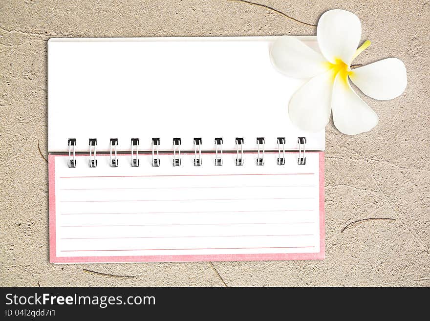 White notebook with frangipani flower on the sand