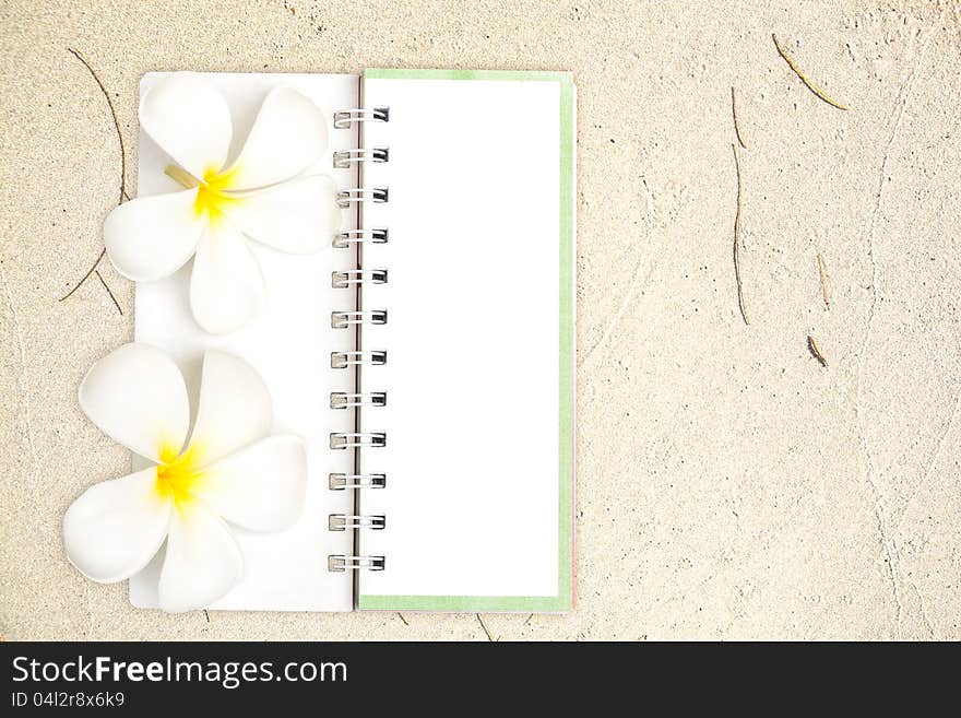 White notebook with white Frangipani flower on the sand