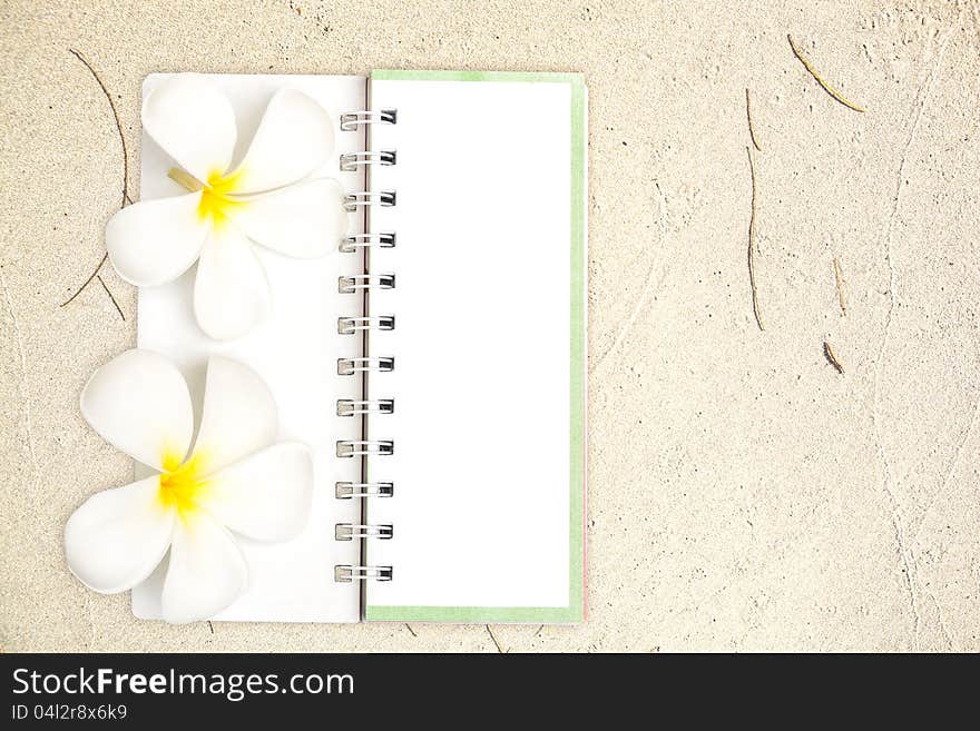 White notebook with frangipani flower on the sand