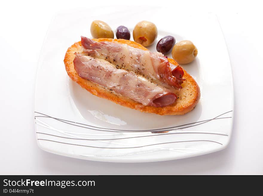 Salami open sandwich with olive on white dish