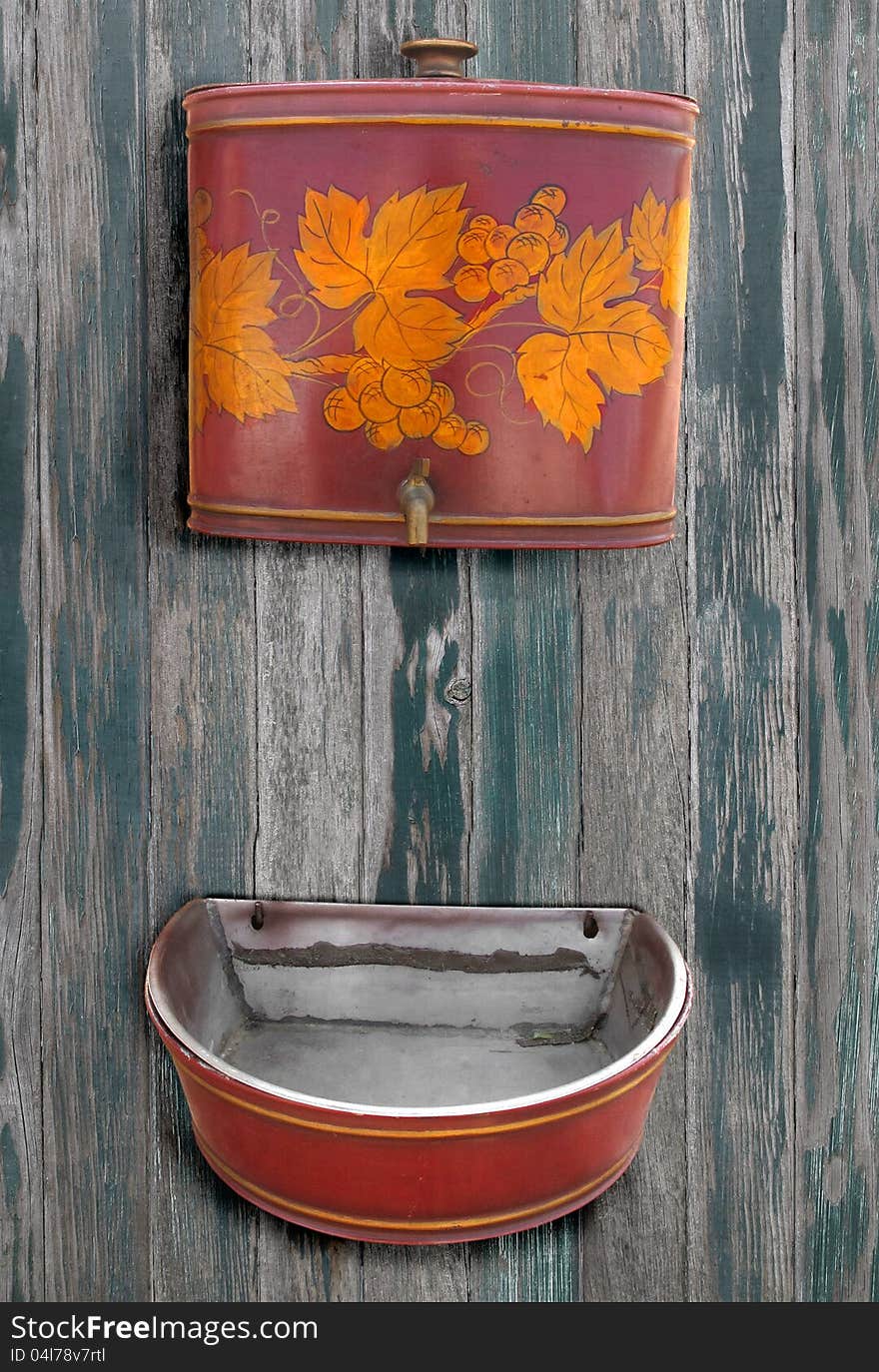 Antique metal sink for hand washing mounted on a wood wall with a metal water reservoir and spout mounted above it. Antique metal sink for hand washing mounted on a wood wall with a metal water reservoir and spout mounted above it.