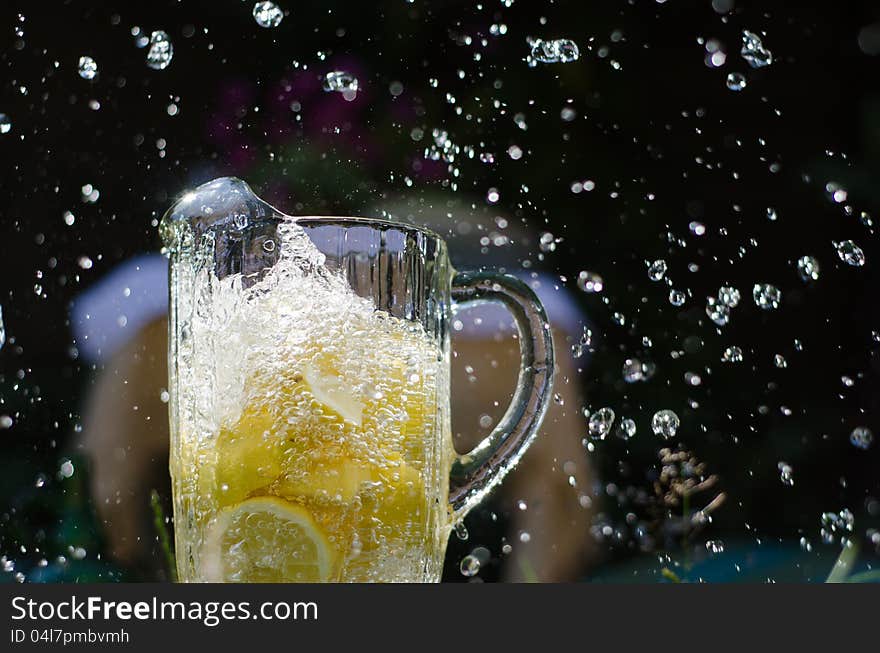 Water pouring and splahing into glass jug filled with lemons on sunny day. Water pouring and splahing into glass jug filled with lemons on sunny day.