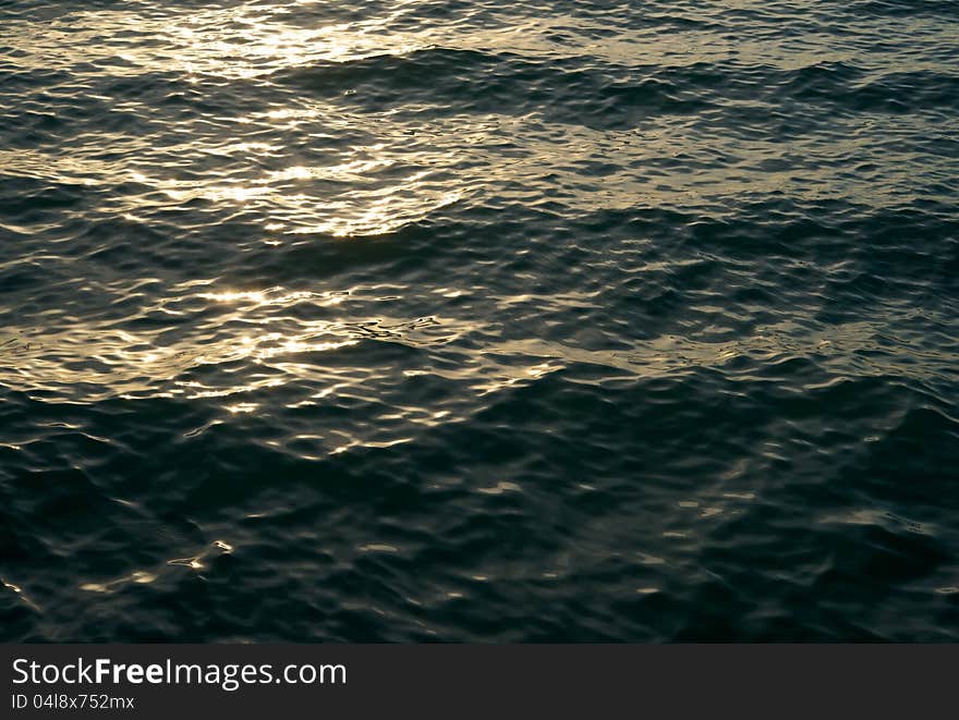 On the surface of the sea play an evening setting sun glare. Shadows on the waves foreshadow the coming night. On the surface of the sea play an evening setting sun glare. Shadows on the waves foreshadow the coming night.