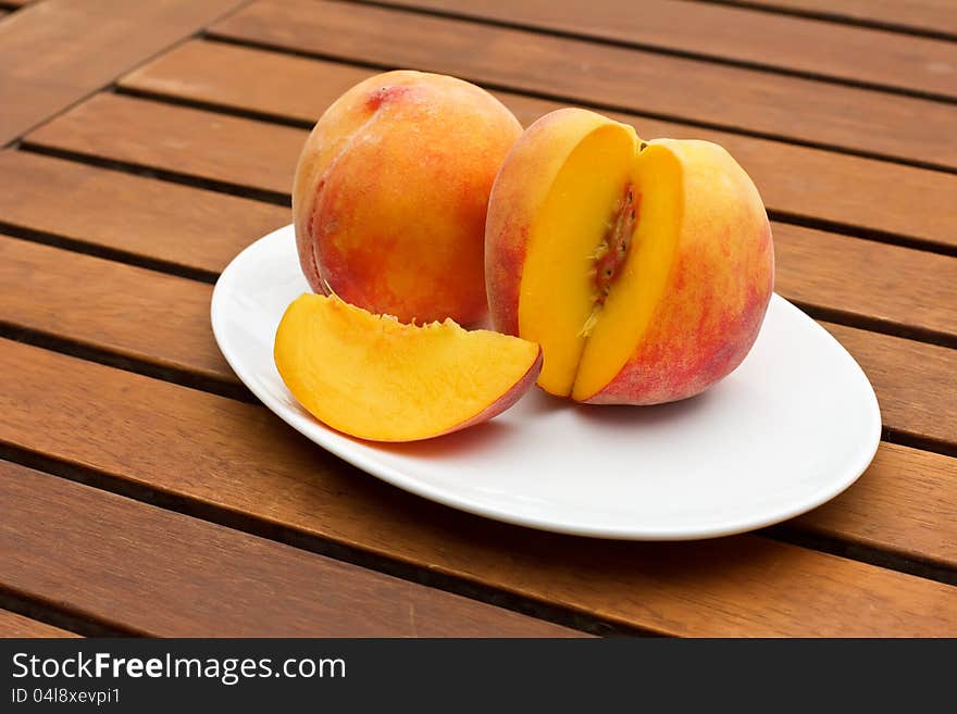 Two fresh peaches on white oval plate on wooden background. Two fresh peaches on white oval plate on wooden background