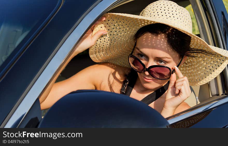 Beautiful female driver in a straw sun hat and sunglasses peering over her glasses checking her side mirror. Beautiful female driver in a straw sun hat and sunglasses peering over her glasses checking her side mirror