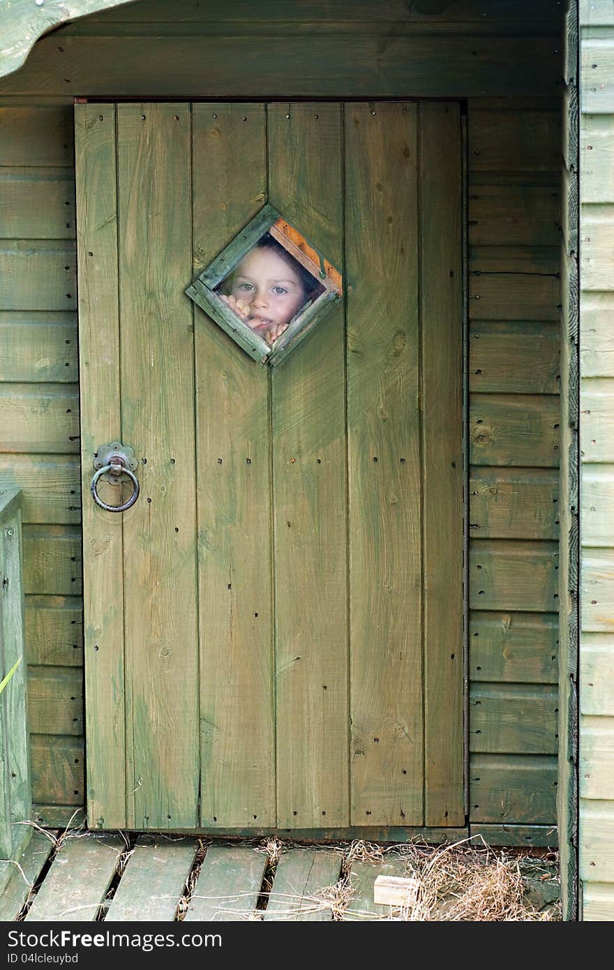 Child boy looking through the small window in a door whilst playing in a wooden garden shed. Child boy looking through the small window in a door whilst playing in a wooden garden shed.