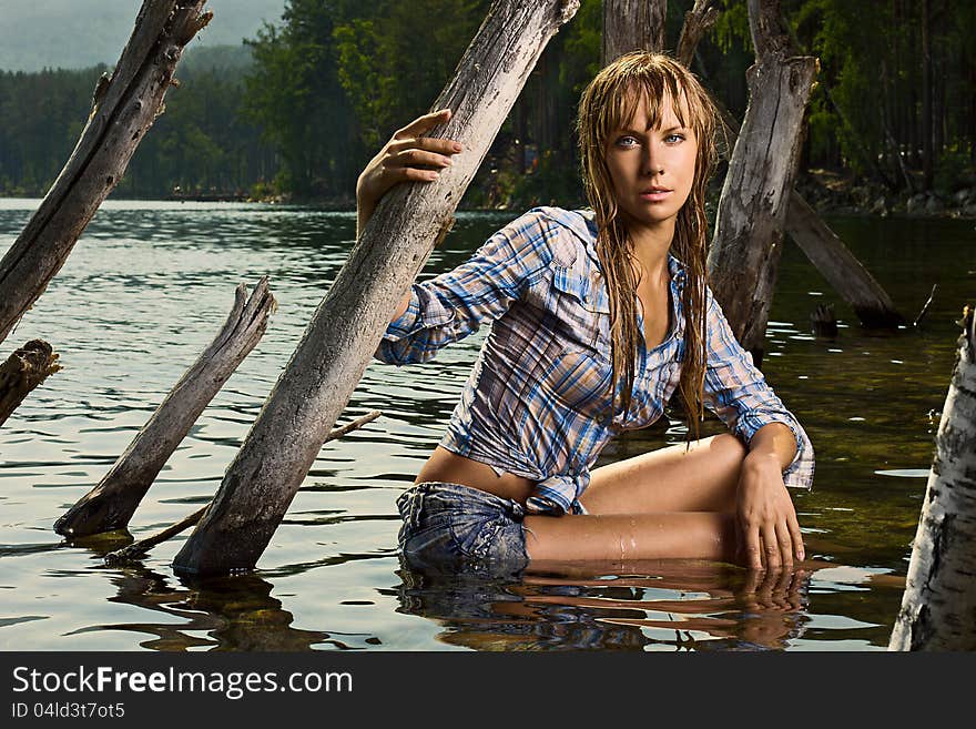 Fashion photo of young beautiful woman sitting in the water and looking at camera? her hair are wet