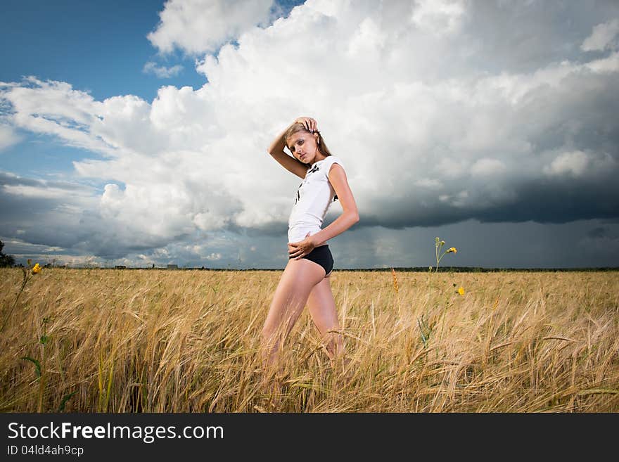 Fashion photo of young beautiful woman standing on a field of wheat against a background of sky and clouds