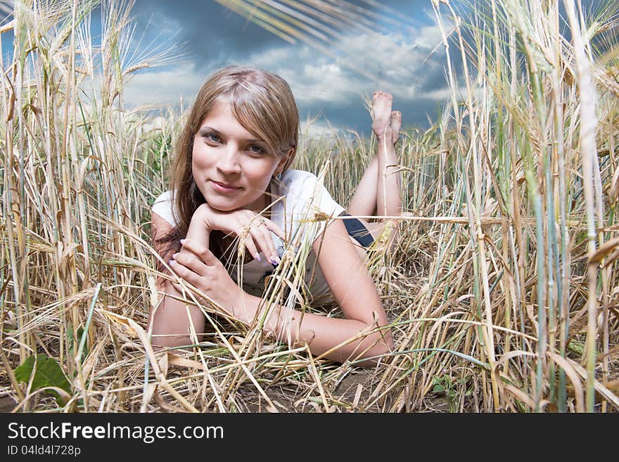 Fashion photo of young beautiful woman lies on a wheat field against a background of sky and clouds