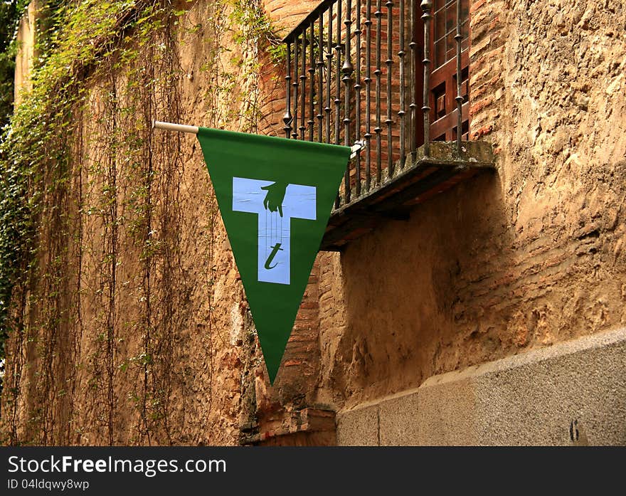 The symbol of the Spanish puppeteers hanging from the balcony of a villa. The green flag depicting a white t shape and a hand with strings marks the location of puppeteers' schools in towns. The symbol of the Spanish puppeteers hanging from the balcony of a villa. The green flag depicting a white t shape and a hand with strings marks the location of puppeteers' schools in towns.