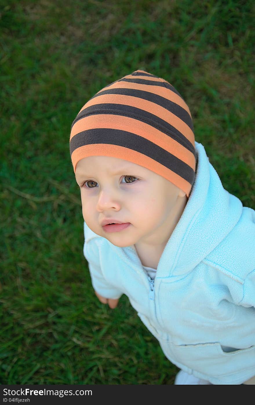 Against green bushes the kid in a sweater and a cap. Against green bushes the kid in a sweater and a cap