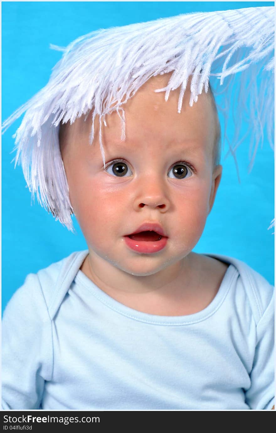 On a blue background a portrait of the child with a big fluffy white feather on the head. On a blue background a portrait of the child with a big fluffy white feather on the head