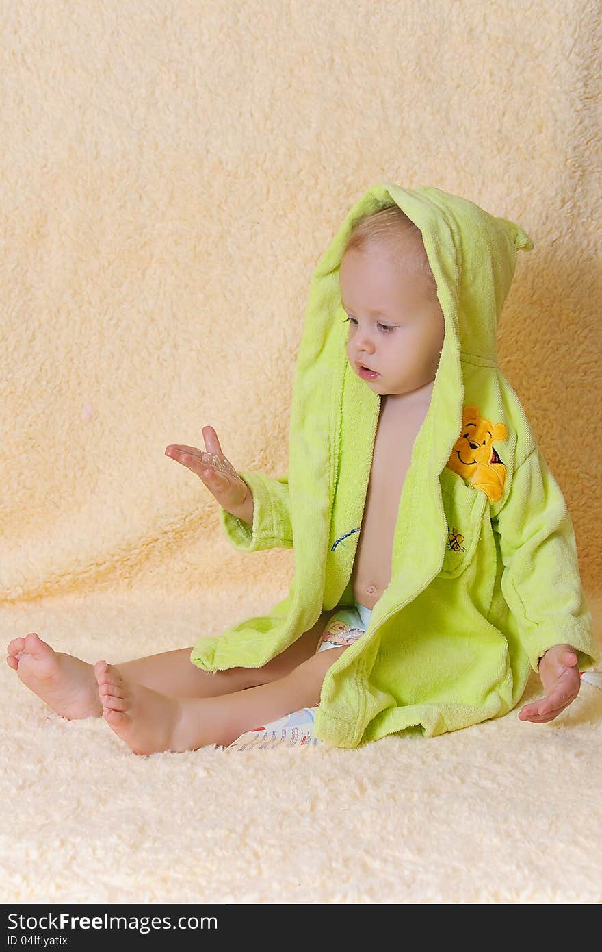 The kid in a bathing dressing gown sits. The kid in a bathing dressing gown sits