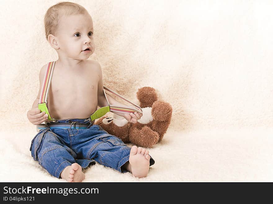 The child sits on a floor with a toy in jeans and barefoot. The child sits on a floor with a toy in jeans and barefoot