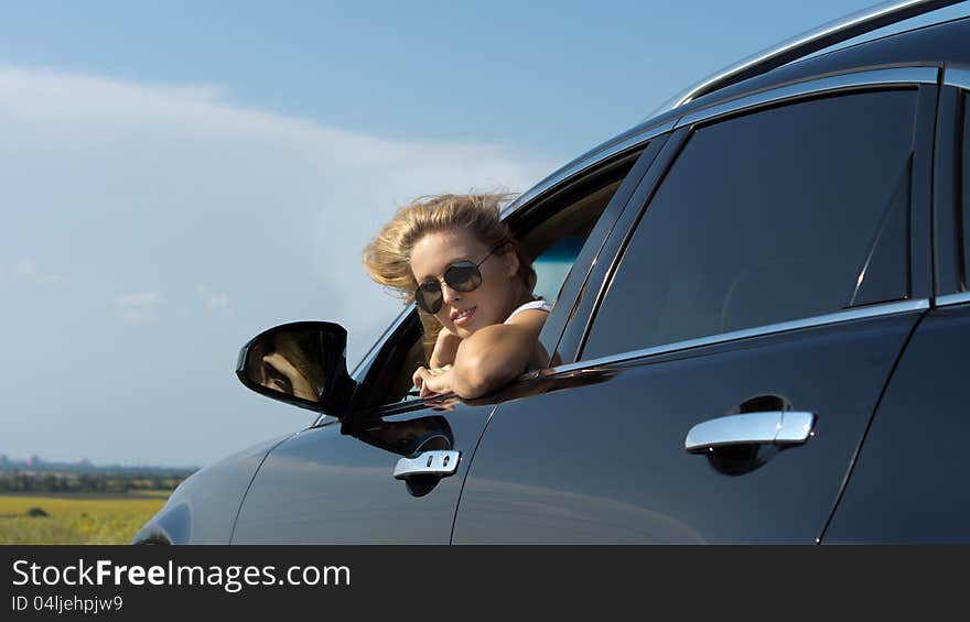 Low angle view of a blonde woman in sunglasses looking back out of a car window. Low angle view of a blonde woman in sunglasses looking back out of a car window