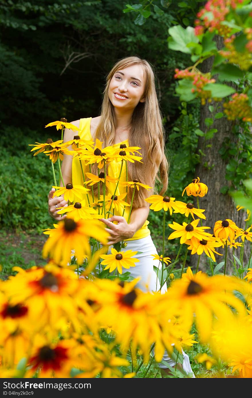 Close-up portrait of a young smiling  woman with yellow flowers against a background of trees. Close-up portrait of a young smiling  woman with yellow flowers against a background of trees