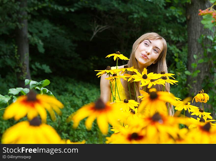 Close-up portrait of a young woman with yellow flowers against a background of trees. Close-up portrait of a young woman with yellow flowers against a background of trees