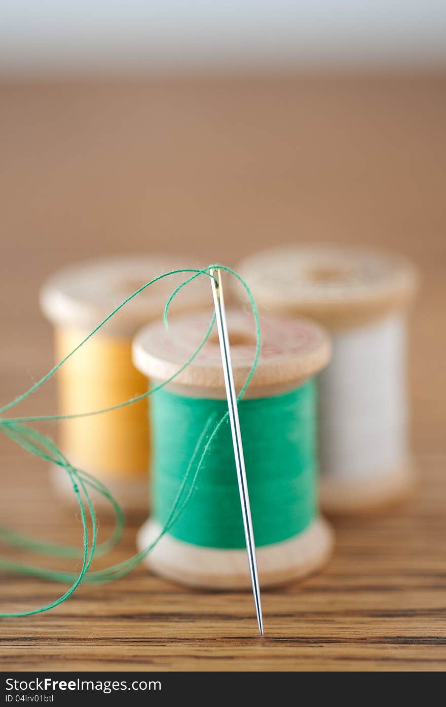 Sewing needle with green thread in front of spools of thread in close focus. Sewing needle with green thread in front of spools of thread in close focus