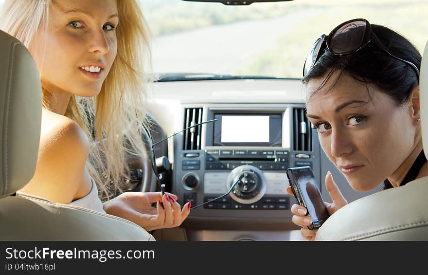 Two attractive women seated in the front seats of a car looking back over their shoulders to the rear of the vehicle. Two attractive women seated in the front seats of a car looking back over their shoulders to the rear of the vehicle