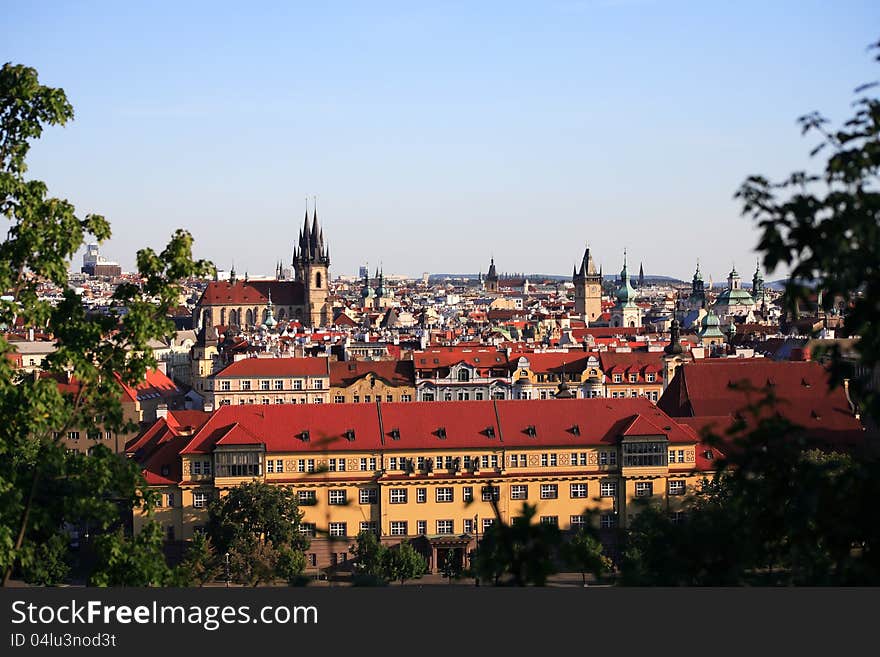 View of red roofs and high gothic towers between green leaves. Prague, Czech Republic. View of red roofs and high gothic towers between green leaves. Prague, Czech Republic