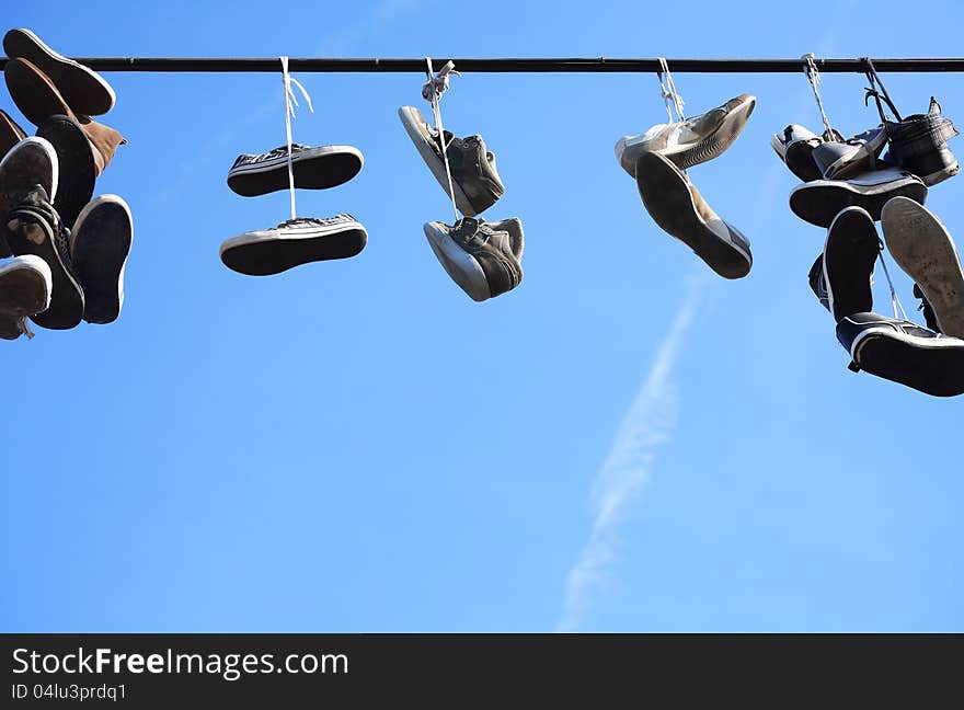 Lot of worn shoes hanging on wire against blue sky