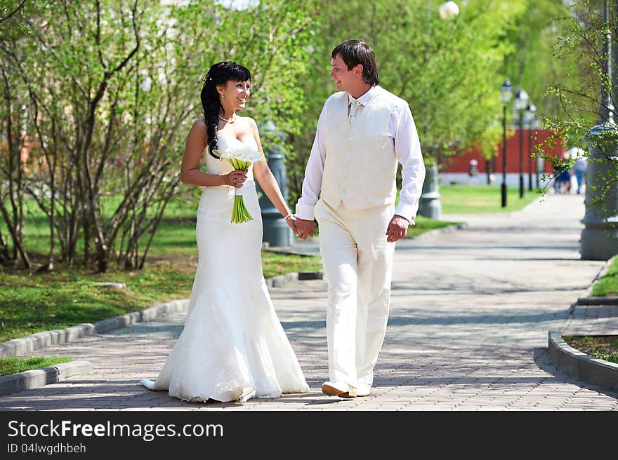 Happy groom and happy bride walking in park