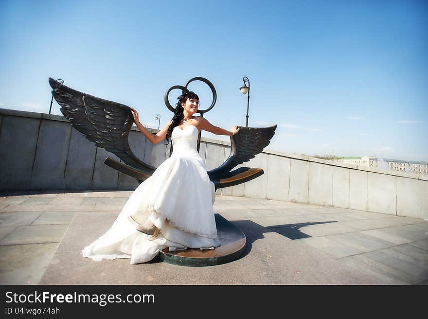 Bride on bronze bench with wings in sunny wedding day