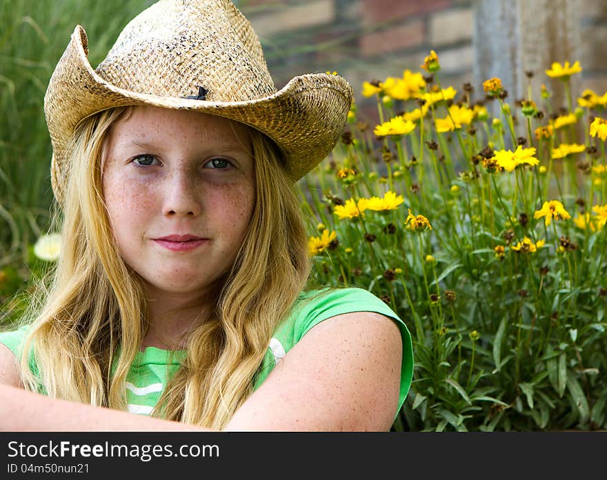 A young pretty girl in a rustic cowboy hat sits near yellow flowers. A young pretty girl in a rustic cowboy hat sits near yellow flowers.