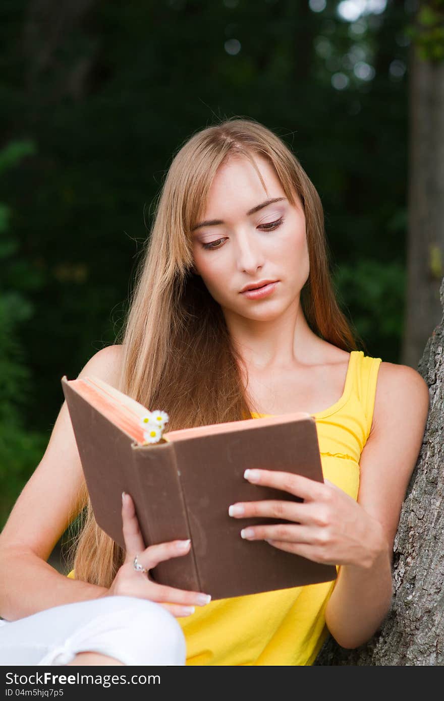 Young woman sitting near the tree and reading a book. Macro. Young woman sitting near the tree and reading a book. Macro