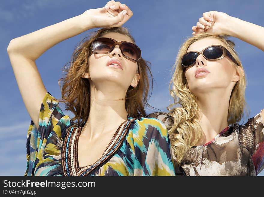 Two beautiful brunette and blonde girl in sunglasses on background blue sky. Two beautiful brunette and blonde girl in sunglasses on background blue sky