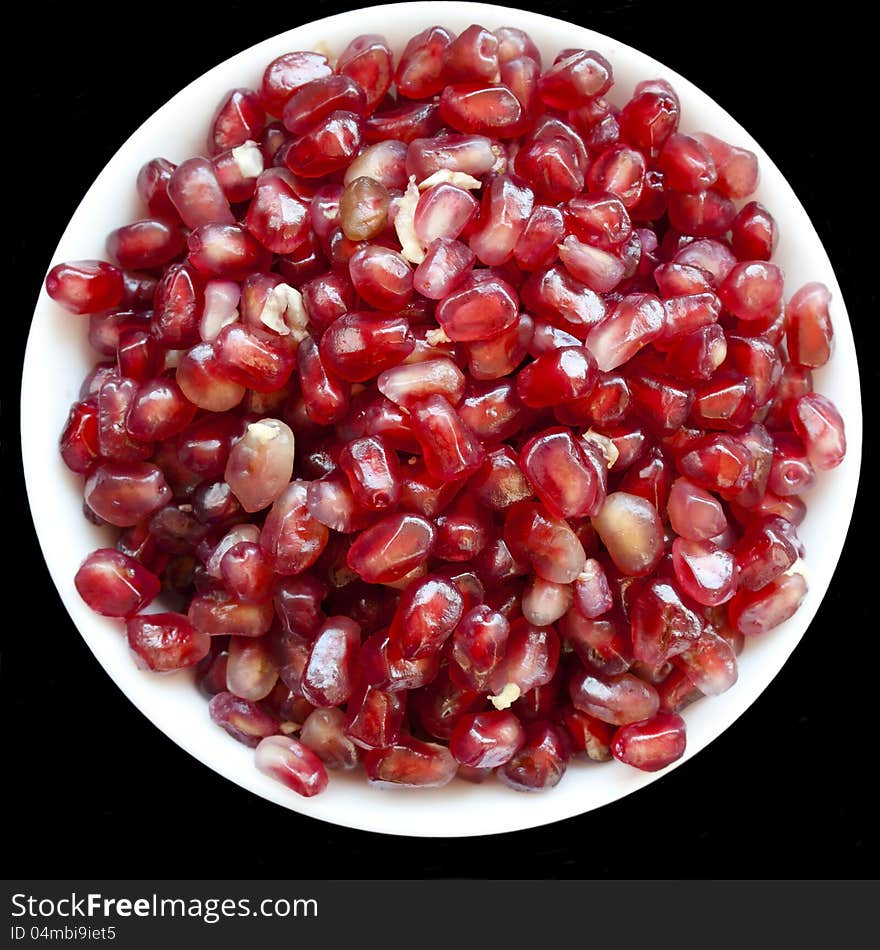 Red grains of pomegranate on white plate over black background