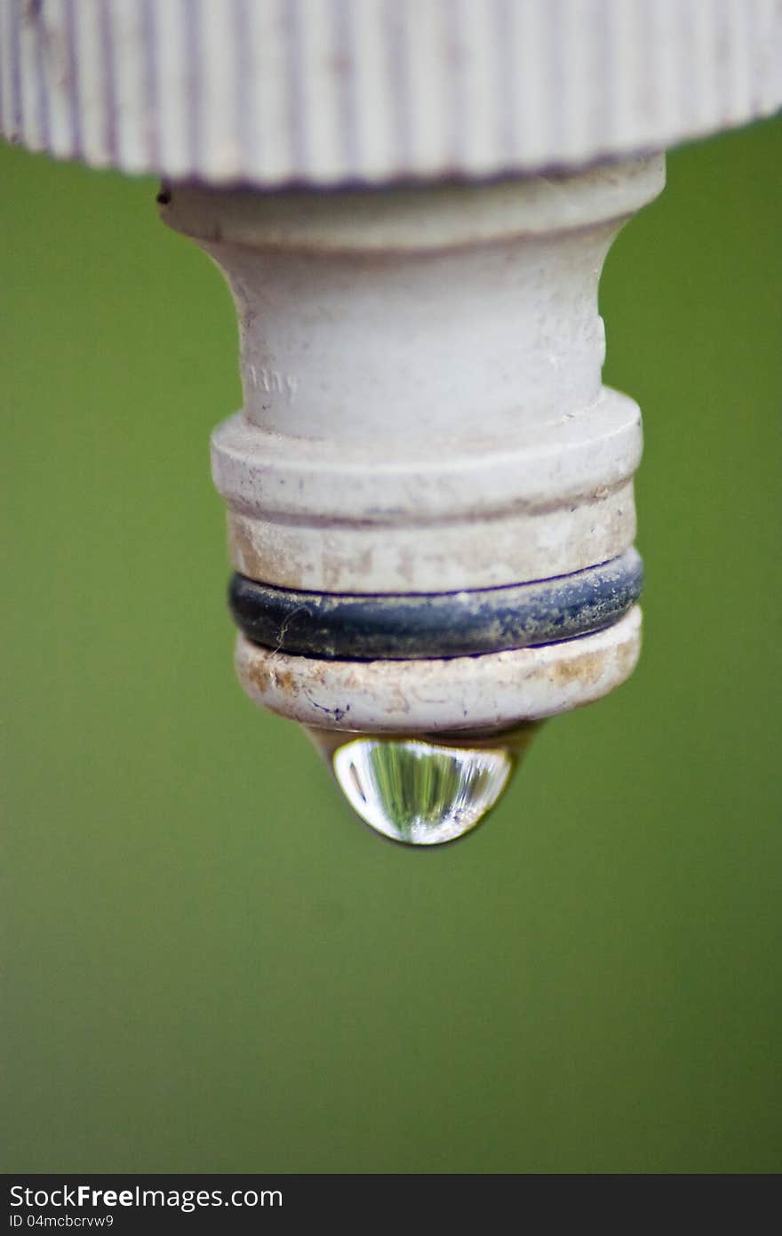 End of a spigot with water drop on it over green background. End of a spigot with water drop on it over green background