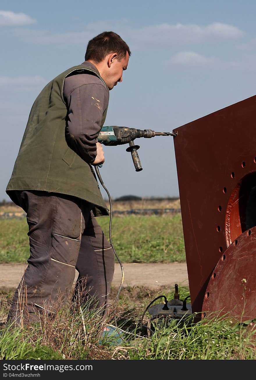 A man drilling a hole in a plate of metal, focus on man