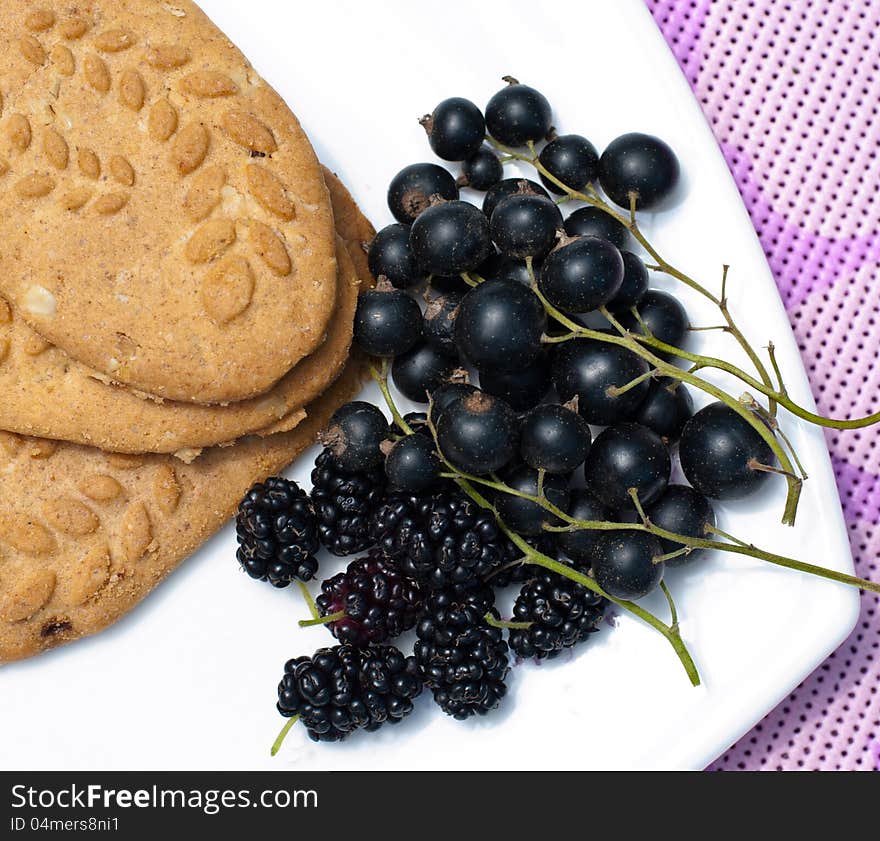 Black currant, mulberry and cereal biscuits on a white plate on a purple table cloth. Black currant, mulberry and cereal biscuits on a white plate on a purple table cloth