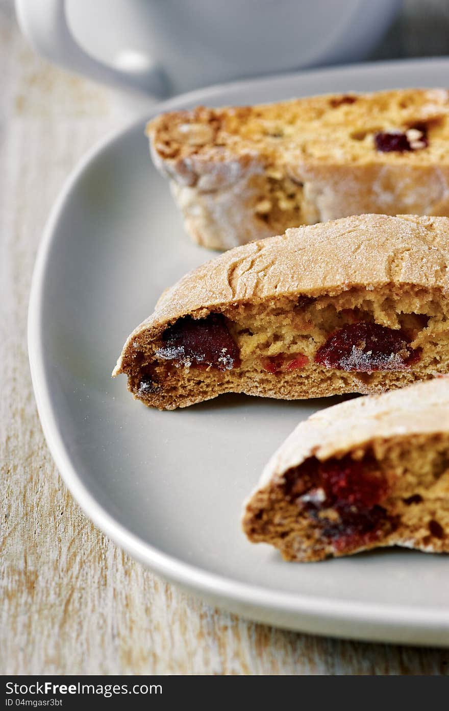 Three slices of almond biscotti biscuits with jam on the plate with a cup in the background