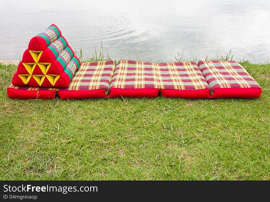 Triangular pillows and mattresses are placed on a beautiful pattern on the grass beside the pond. Triangular pillows and mattresses are placed on a beautiful pattern on the grass beside the pond.