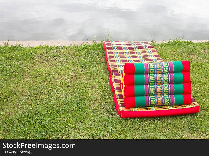 Triangular pillows and mattresses are placed on a beautiful pattern on the grass beside the pond. Triangular pillows and mattresses are placed on a beautiful pattern on the grass beside the pond.