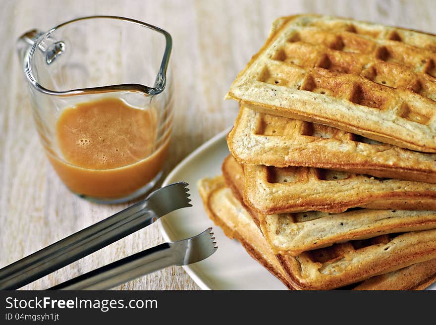 Stack of homemade waffles on the plate with a cup of brown syrup