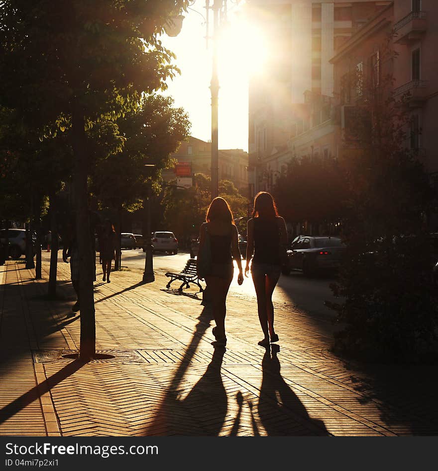 Two women walking in the sun ray, in the city.