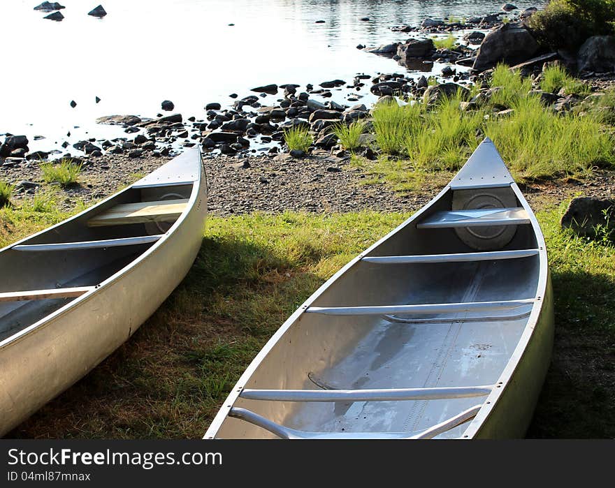 A duo of canoes, set at the edge of the lake and waiting to get out on the water again. A duo of canoes, set at the edge of the lake and waiting to get out on the water again.