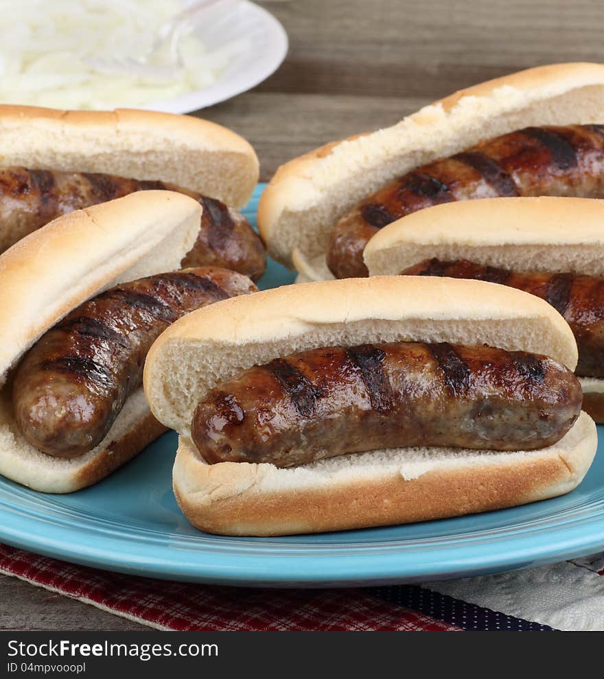 Platter of grilled bratwursts on buns with onions in background