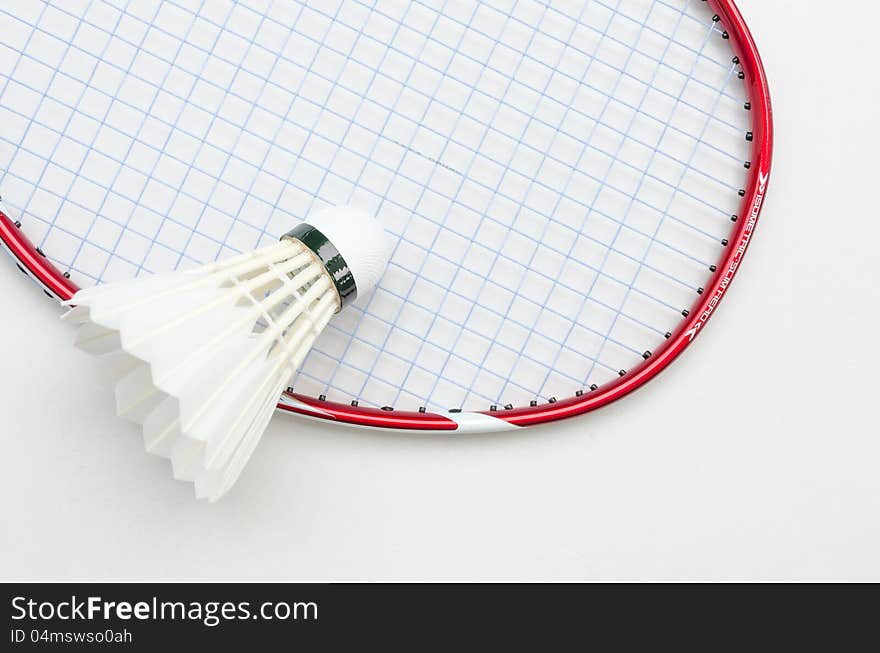 Badminton racket in red color and light blue string with shuttlecock in top right partial angle view on white background. Badminton racket in red color and light blue string with shuttlecock in top right partial angle view on white background